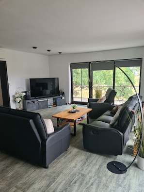 A modern living room with a sofa set, a coffee table, a TV, and a large window with a view of greenery. - Apartment 'Penthouse Steinhude' with Private Terrace, Wi-Fi and Air Conditioning (Wunstorf)