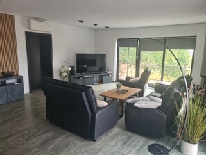 A modern living room with a flat-screen TV, black sofas, a wooden coffee table, and a balcony with a view of greenery. - Apartment 'Penthouse Steinhude' with Private Terrace, Wi-Fi and Air Conditioning (Wunstorf)