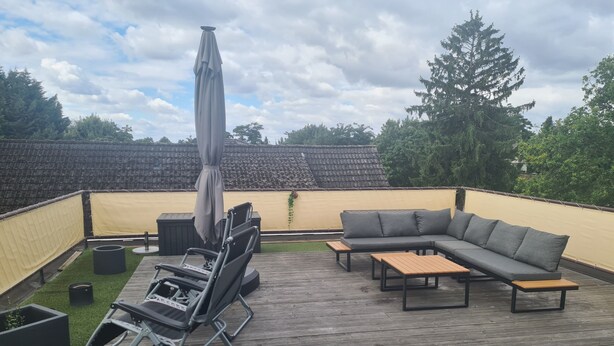 Eine Terrasse im Freien mit einem grauen Ecksofa, einem Klappstuhl und einem Tisch.