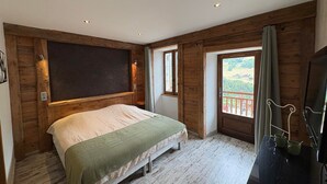 A bedroom with a bed, wooden walls, a balcony with a view, and a TV on a stand. - Splendid alpine apartment - 10 guests (Les Saisies)