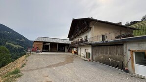 A two-story building with a garage, a covered outdoor area, and a view of a hilly landscape. - Splendid alpine apartment - 10 guests (Les Saisies)