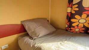 Uma cama de solteiro com cabeceira, travesseiro e cobertor em quarto com parede lisa e tomada.
