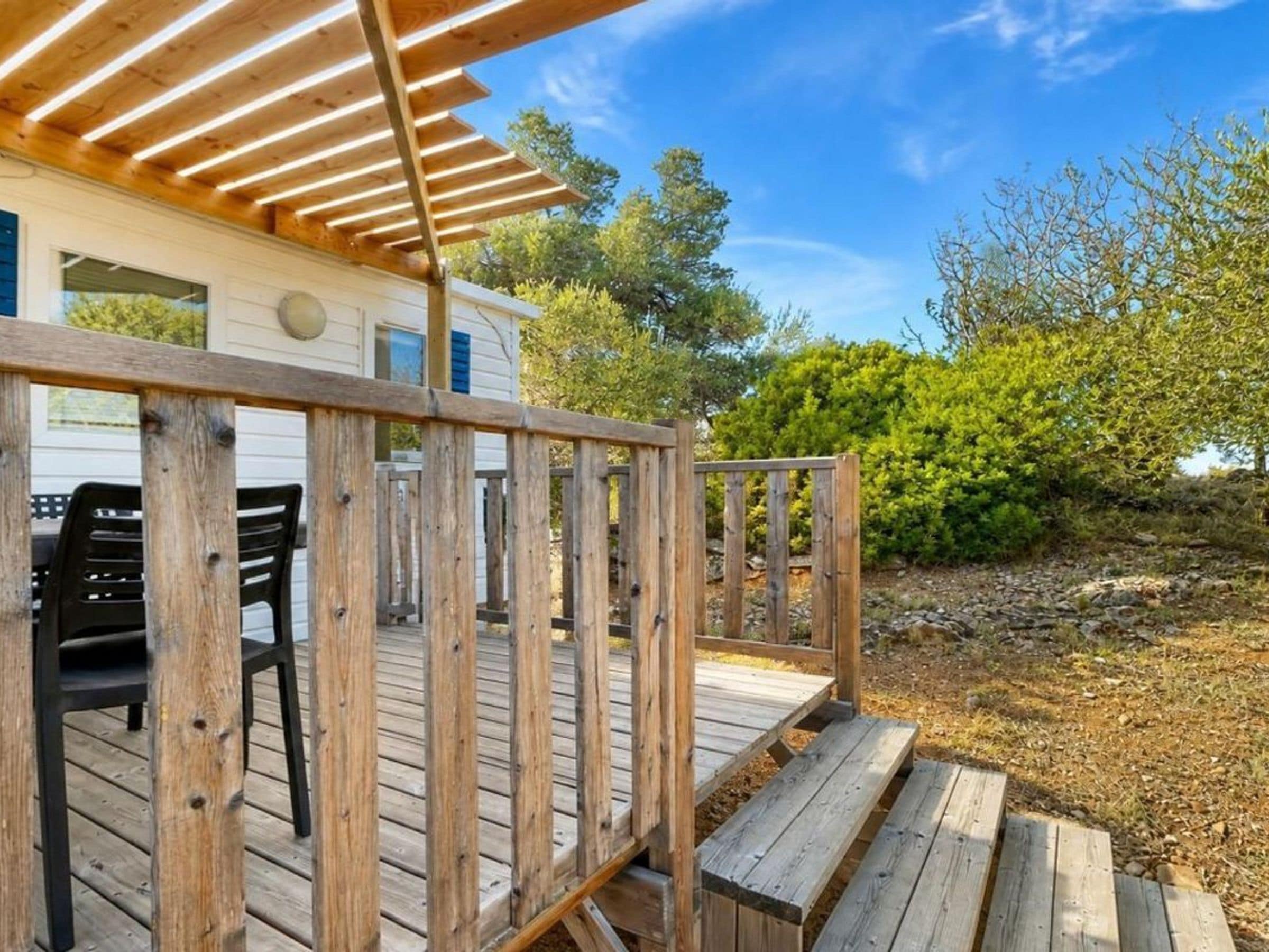 A wooden deck with outdoor seating, a covered area, and a view of a white building with blue shutters.