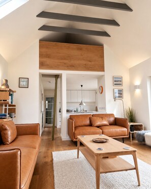 Ein geräumiges Wohnzimmer mit einem braunen Ledersofa, einem Holztisch und einer Küchenzeile im Hintergrund.