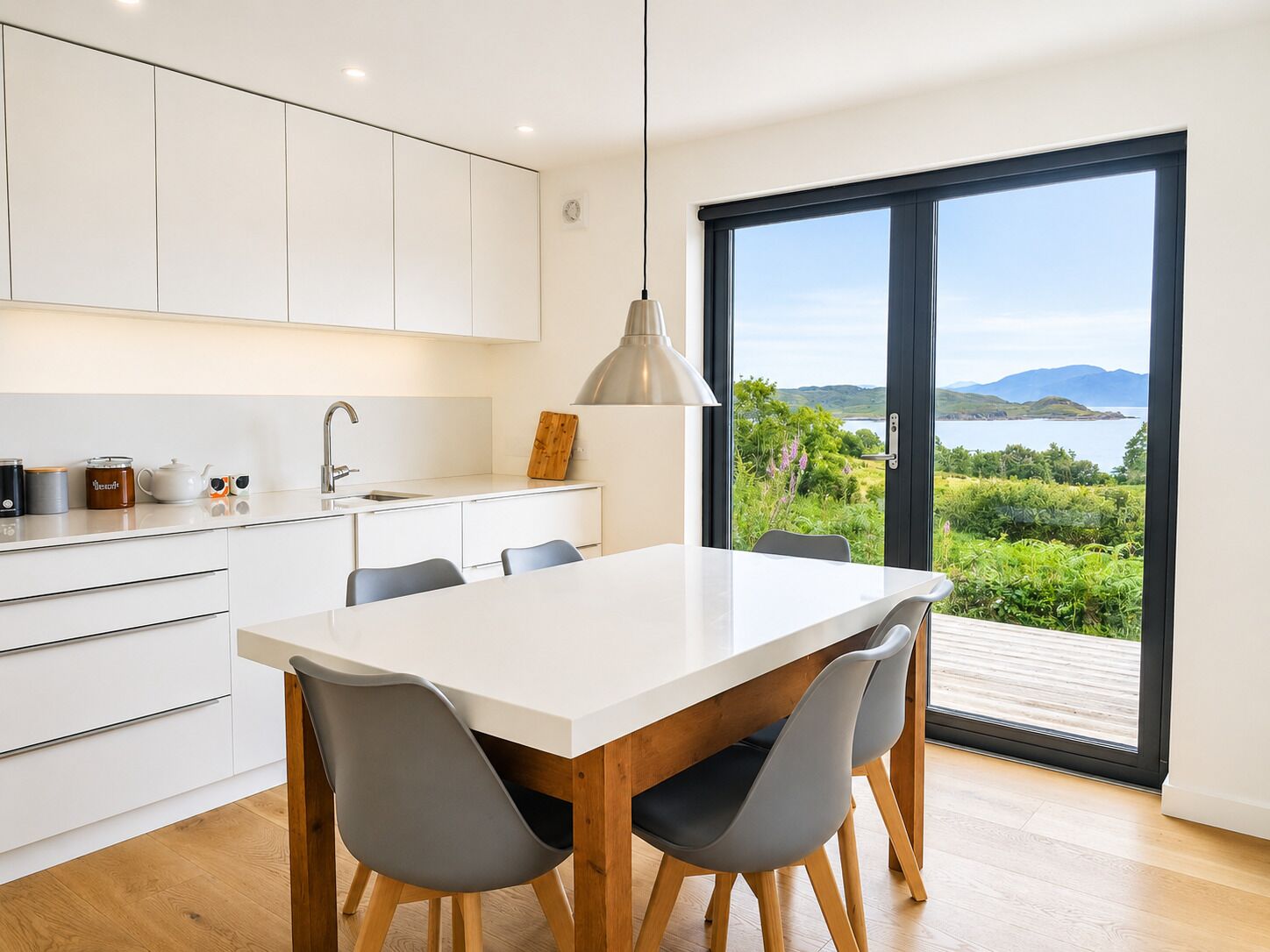 A modern kitchen with a large dining table, white cabinets, and a view of the outdoors.