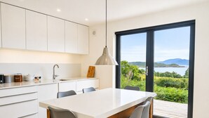Eine moderne Küche mit großem Esstisch, weißen Schränken und Blick ins Freie.