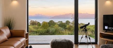 A living room with a large sliding glass door leading to a scenic view of a lake and mountains.