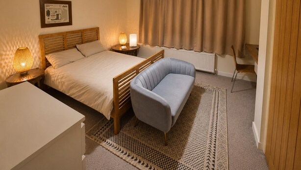 Ein Hotelzimmer mit Bett, Nachttischlampen, Schreibtisch, Stuhl, einem gemusterten Teppich und einem Vorhang.
