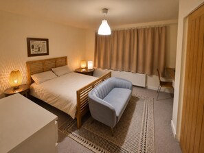 Une chambre d’hôtel avec un lit, des lampes de chevet, un bureau, une chaise, un tapis à motifs et un rideau.