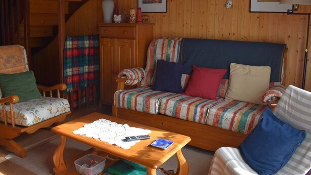 A cozy living room with a wooden staircase, a sofa with colorful cushions, a small table with a remote control, and framed artwork on the wall. - Chalet with fireplace, Pyrenees view - 5 guests (Font-Romeu-Odeillo-Via)