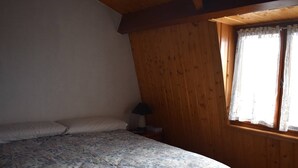 A bedroom with a bed, pillows, a nightstand, a lamp, and a window with lace curtains. - Chalet with fireplace, Pyrenees view - 5 guests (Font-Romeu-Odeillo-Via)
