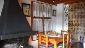 A dining area with a table and chairs, a black grill, lace curtains, and a wall with a framed picture. - Chalet with fireplace, Pyrenees view - 5 guests (Font-Romeu-Odeillo-Via)