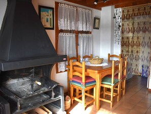 Ein Essbereich mit Tisch, Stühlen, einem schwarzen Grill, Spitzenvorhängen und einem Wandbild.