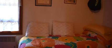 Une chambre à coucher avec un lit, deux tableaux encadrés accrochés au mur, une fenêtre avec un rideau et un objet suspendu au mur.