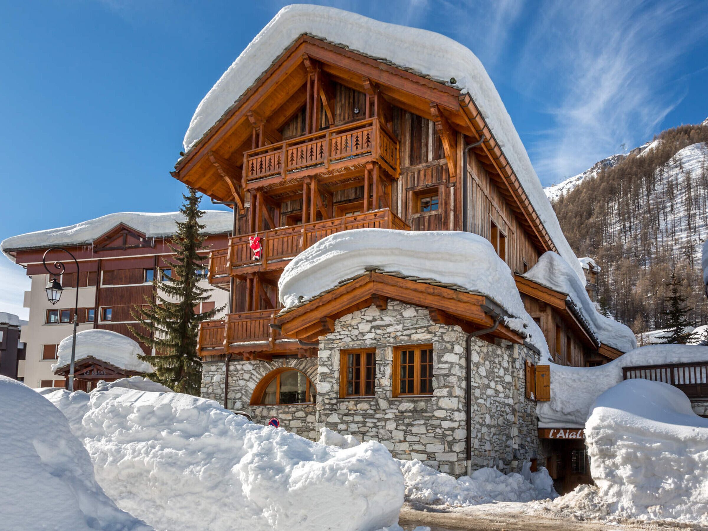A chalet-style building with a stone facade and wooden balconies, surrounded by snow.