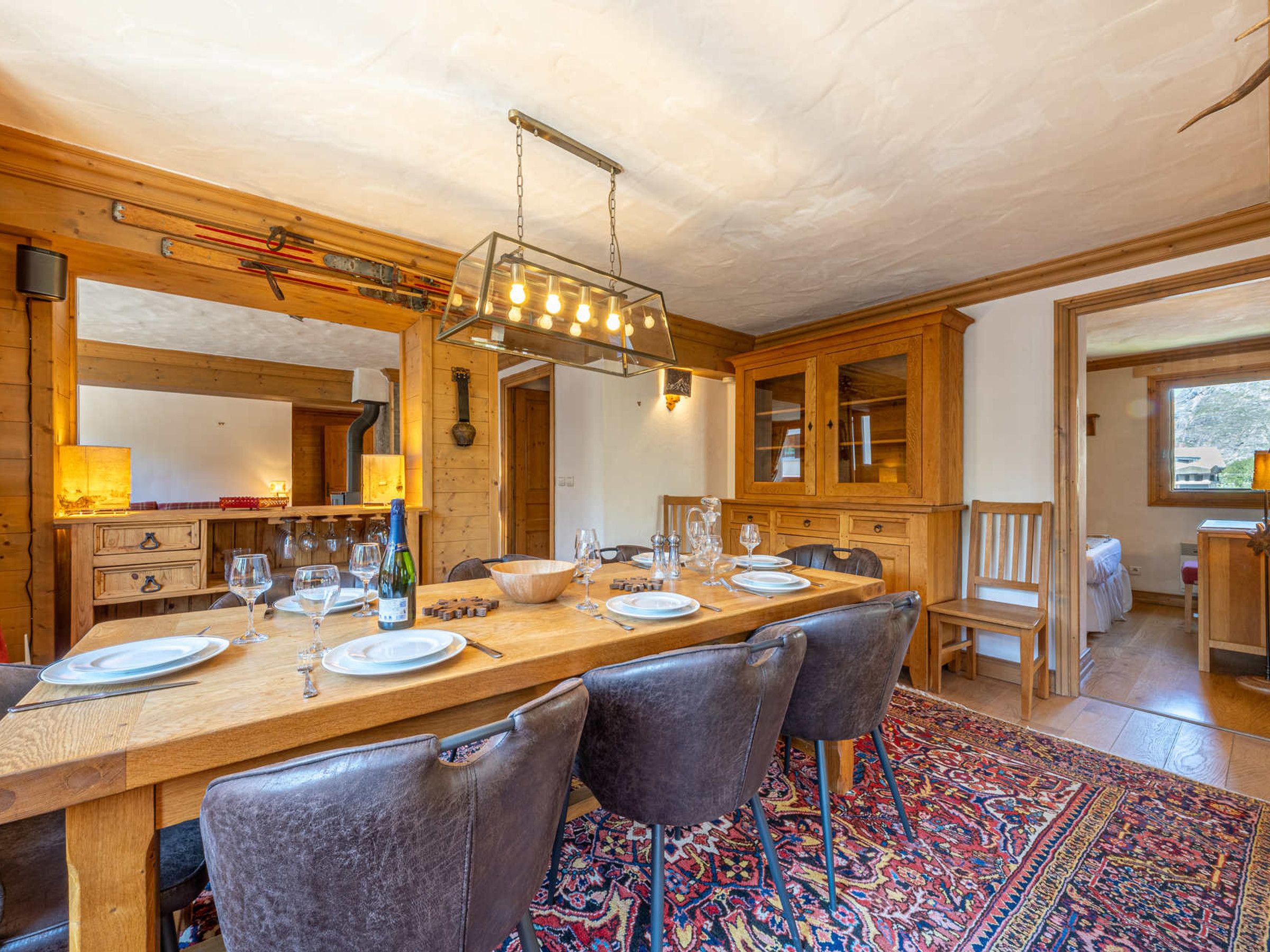 A wooden dining room with a long table set for a meal, surrounded by chairs.