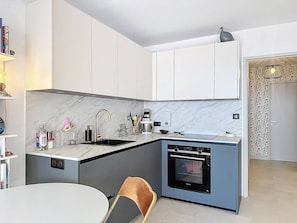 A modern kitchen with a built-in oven, a sink, and a dining area with a table and chair. - Apartment sea view, pool, AC - 4 guests (Le Lavandou)