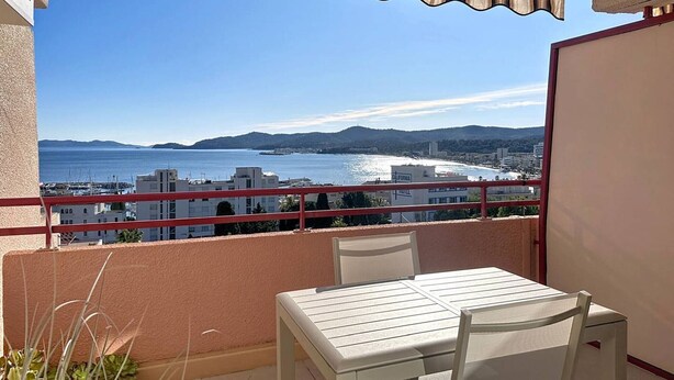 Ein Balkon mit Tisch und Stühlen, der Blick auf die Küste mit Gebäuden und einem klaren Himmel bietet.