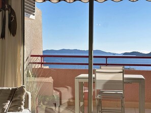 A balcony with a table and chairs, overlooking a body of water and distant landforms. - Apartment sea view, pool, AC - 4 guests (Le Lavandou)