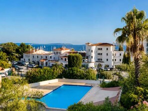 A hotel with a swimming pool surrounded by lush greenery and a view of the sea. - Apartment sea view, pool, AC - 4 guests (Le Lavandou)