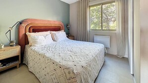 Ein Schlafzimmer mit einem Bett, Nachttischen, einem Fenster mit Vorhängen und einem Heizkörper.