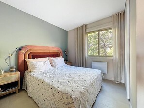 A bedroom with a bed, bedside tables, a window with curtains, and a radiator. - Apartment sea view, pool, AC - 4 guests (Le Lavandou)