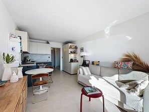 A modern living space with a kitchen, dining area, and a sofa with a side table. - Apartment sea view, pool, AC - 4 guests (Le Lavandou)