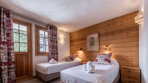 Ein Zimmer mit zwei Einzelbetten, einer Holzwand, einem Fenster mit Vorhängen und einer Wandleuchte.