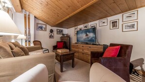 Ein gemütliches Wohnzimmer mit Holzbalken, einem Fernseher und verschiedenen gerahmten Bildern an der Wand.
