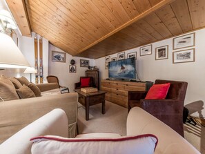 A cozy living room with wooden ceiling beams, a television, and various framed pictures on the wall. - Spacious chalet near slopes - 10 guests (Courchevel)