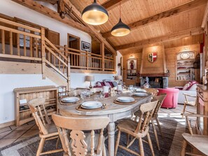 L’intérieur est en bois et comprend une table à manger pour six personnes, entourée de chaises en bois. Un escalier avec des rampes en bois mène à un niveau supérieur.