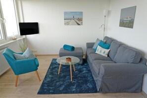 Ein modernes Wohnzimmer mit einem grauen Sofa, einem blauen Sessel, einem Glastisch und einem blauen Teppich.