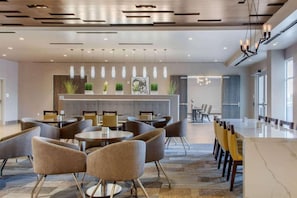 Una hall d'hotel moderna con tavoli e sedie rotonde, una reception e una sala da pranzo con un tavolo lungo.