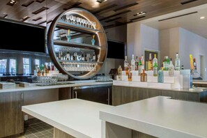 Uma área de bar com prateleira circular exibindo copos e garrafas, bancada branca e design de interiores moderno.