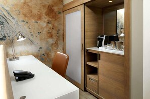 Quarto de hotel com escrivaninha, cadeira, luminária, cafeteira e guarda-roupa.
