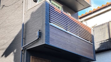 A modern two-story building with a wooden door, a small balcony with a railing, and a visible mailbox.