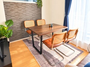 A dining area with a wooden table, four wicker chairs, a grey rug, and a potted plant. - MSTAY Ikebukuro One (Toshima-ku)