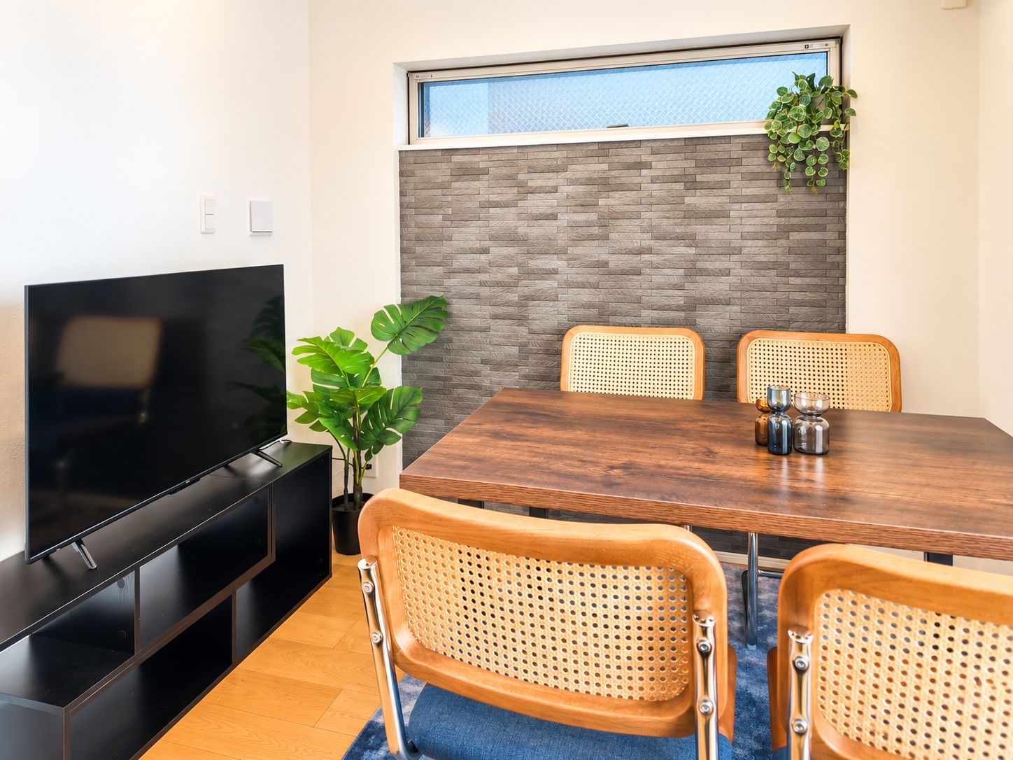 Un comedor moderno con una mesa de madera, dos sillas de mimbre, un televisor y una planta.