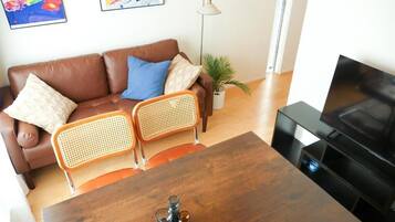 A living room with a brown leather sofa, two wicker chairs, a wooden coffee table, and a television.