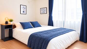 A neatly made bed with a white and blue bedspread, a bedside lamp, and a small plant on a nightstand.