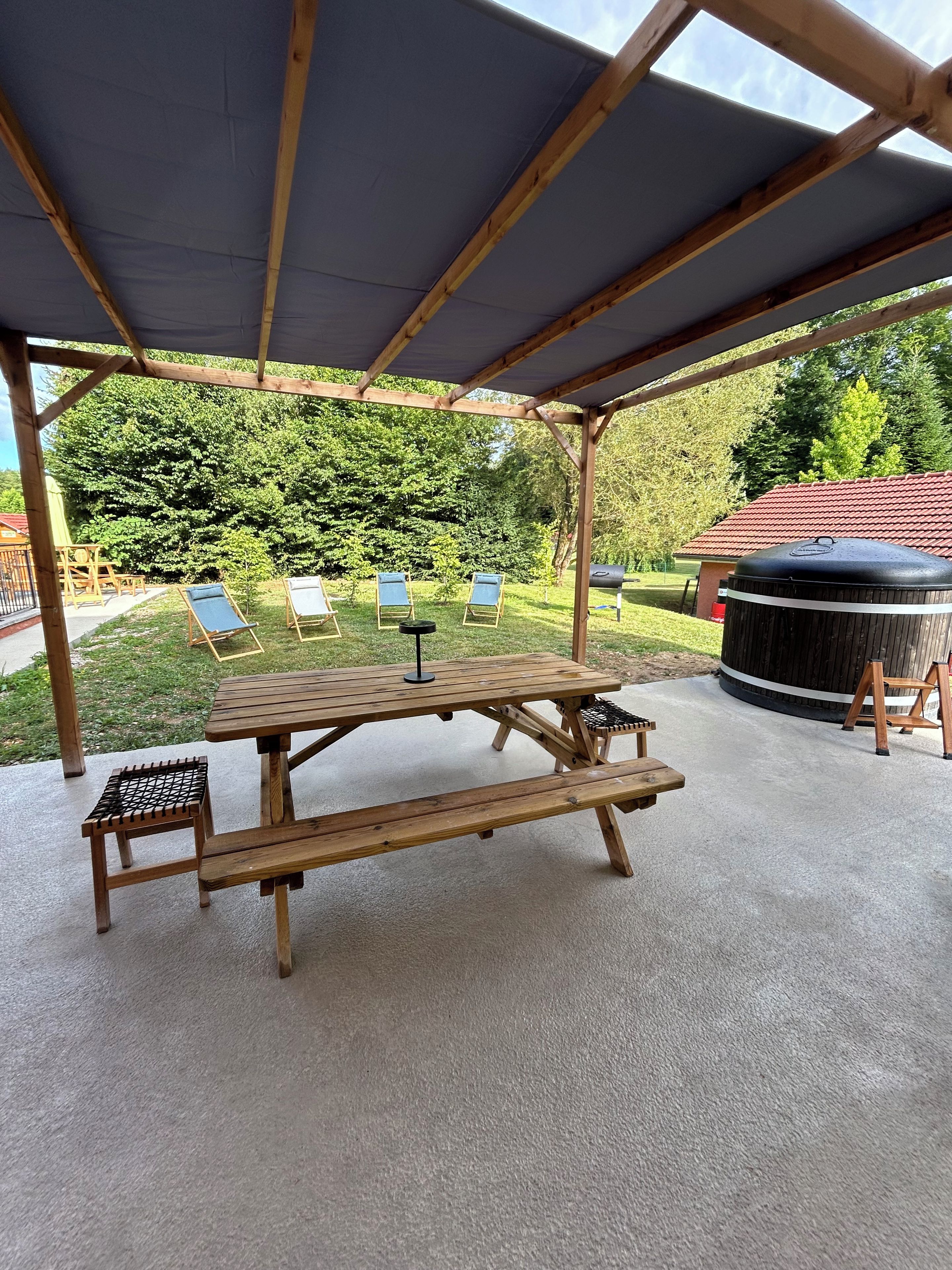 A covered outdoor area with a picnic table, lounge chairs, and a hot tub.