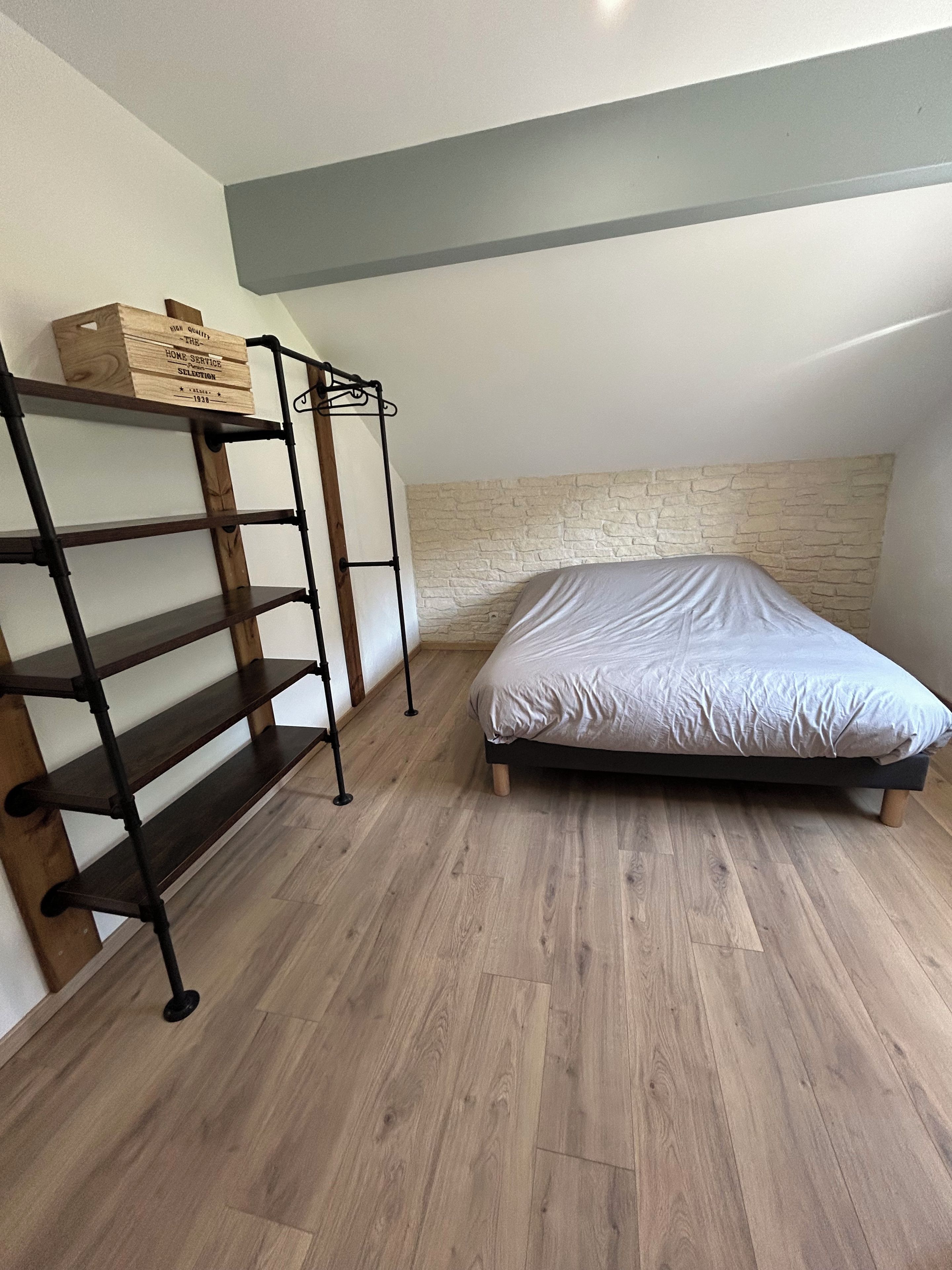 Une chambre avec un lit, une étagère en bois et un mur à la texture rappelant la pierre.