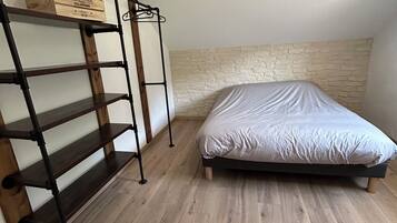 Une chambre avec un lit, une étagère en bois et un mur à la texture rappelant la pierre.