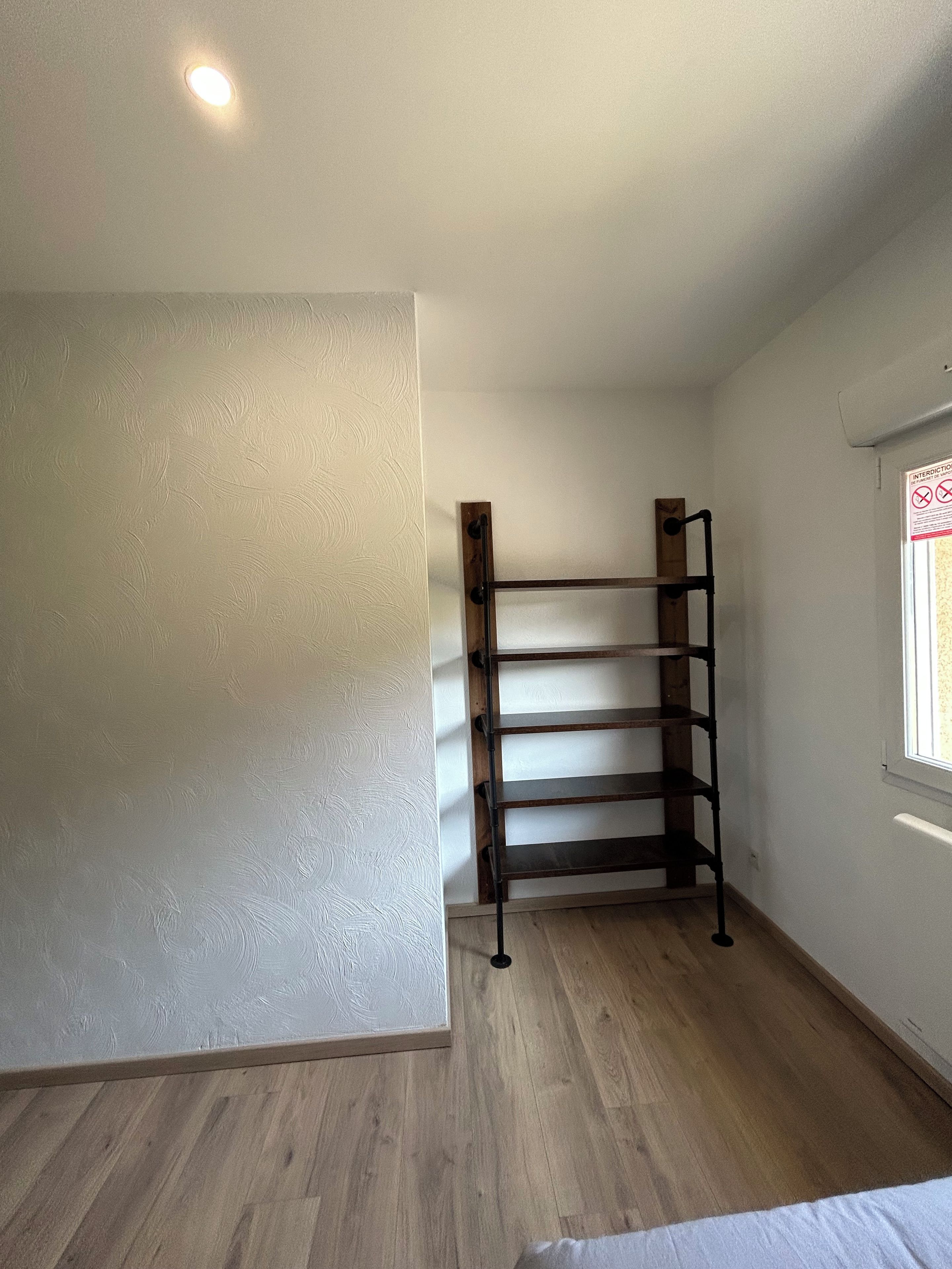Une pièce avec un plancher en bois, un étagère en métal et une fenêtre donnant sur un paysage agréable.