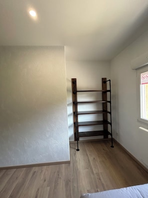 Quarto com piso de madeira, suporte de metal e janela com vista.