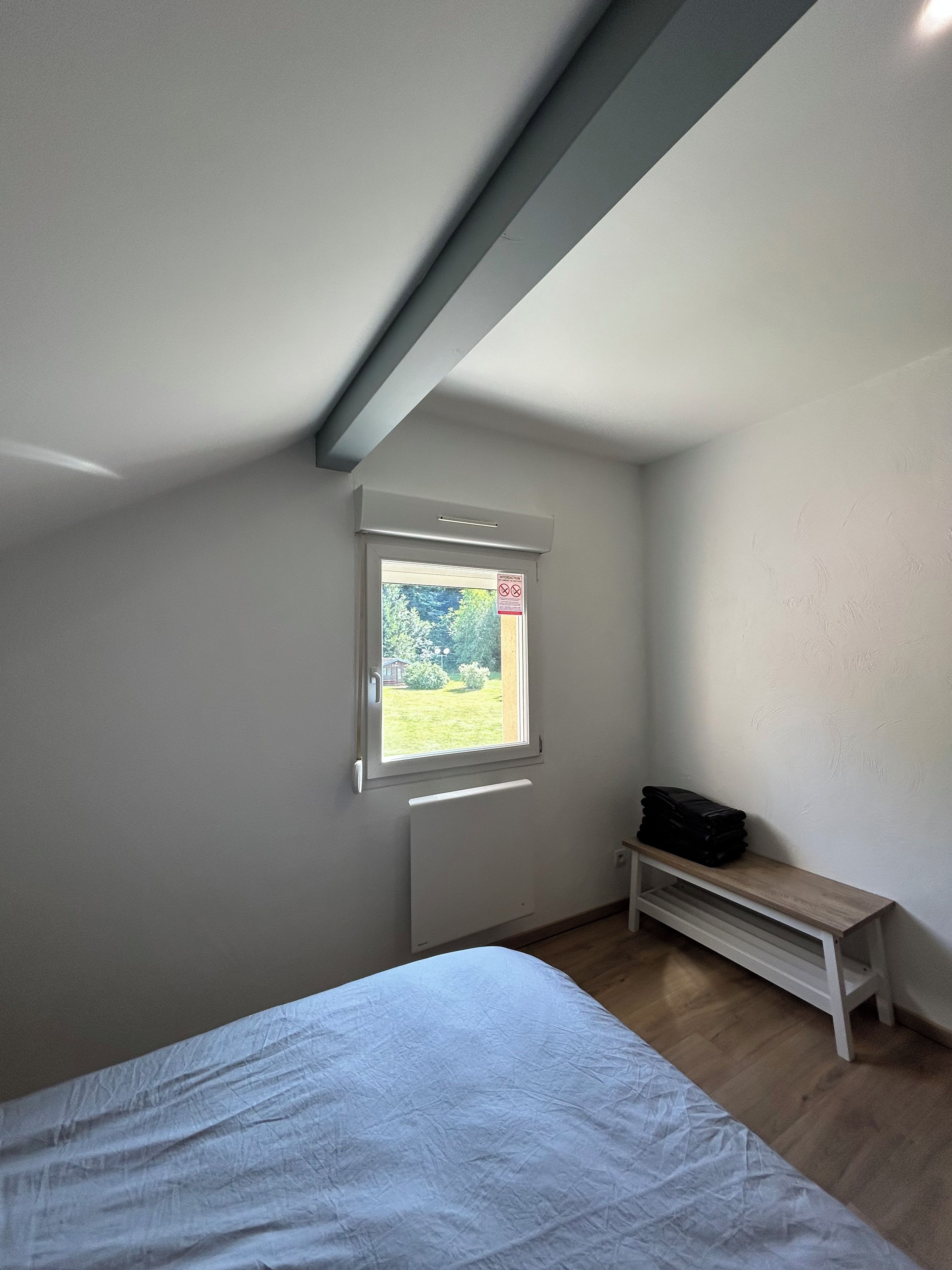 A bedroom with a bed, a window, a radiator, and a bench.