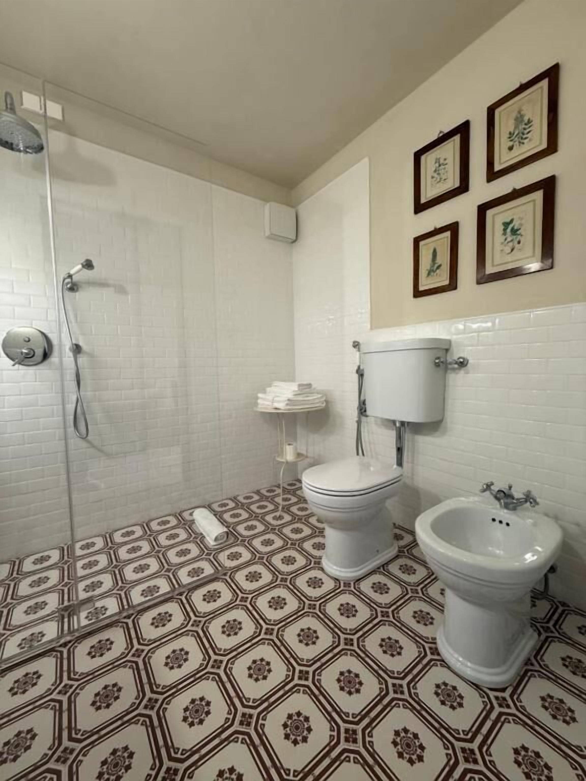 Een badkamer met douche, toilet, bidet en vloertegels met een patroon.