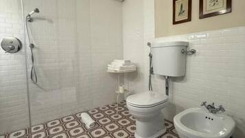 Een badkamer met douche, toilet, bidet en vloertegels met een patroon.