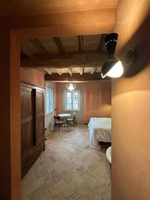 A narrow hallway with a wooden door, a small table with chairs, a bed, and a window with natural light.