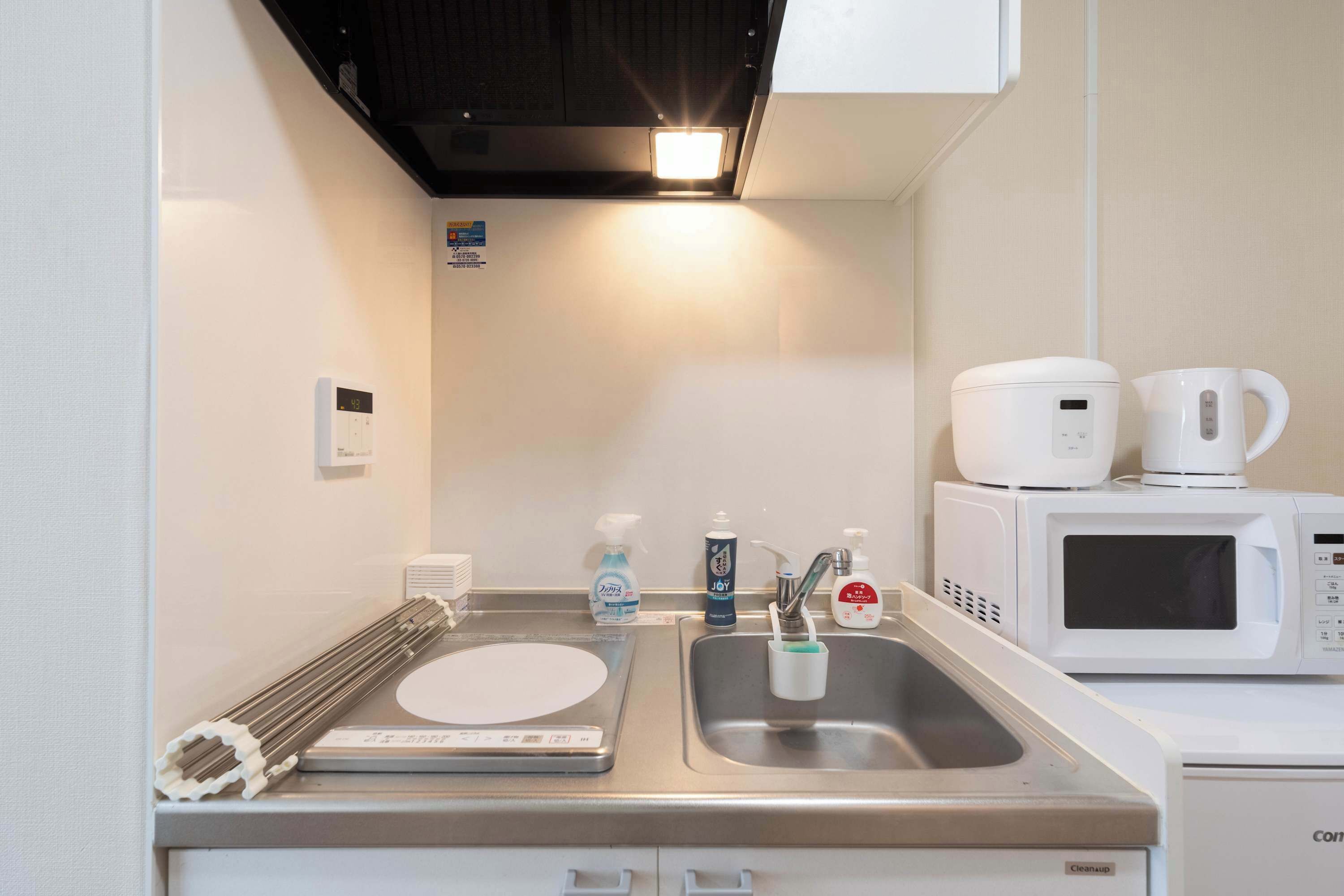 A compact kitchenette with a microwave, coffee maker, and a sink with hand soap and a toothbrush.